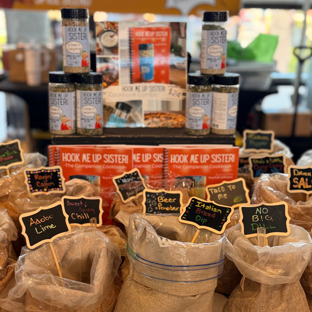 Hook Me Up Sister spice jars and cookbook display with labeled spice blend bags at the farmers market